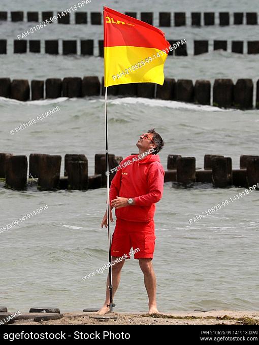 25 June 2021, Mecklenburg-Western Pomerania, Ahrenshoop: An employee of the water rescue service of the German Life Saving Association DLRG puts up a flag on...
