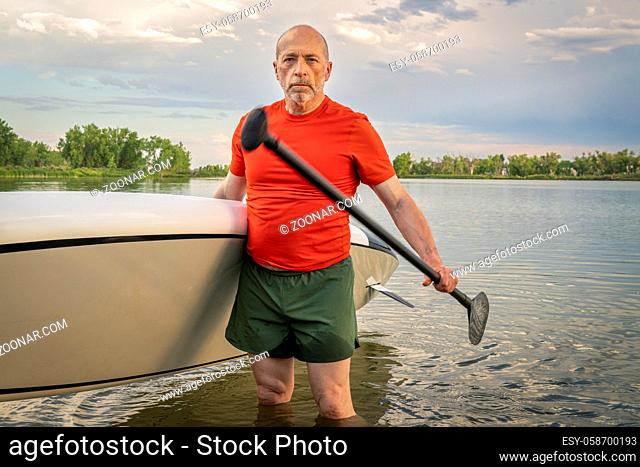 Environmental portrait of a senior paddler with his stand up paddleboard on a lake shore in Colorado