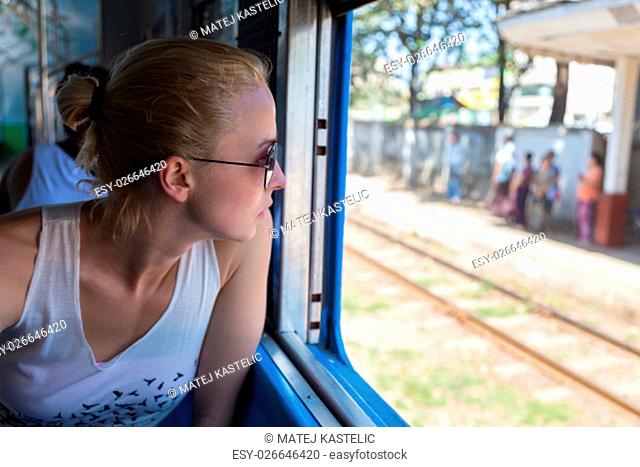 Young female adventurer traveling by train in Asia, waching local people through big window
