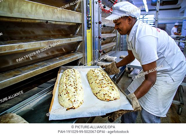 18 October 2019, Saxony, Dresden: Moussa Duale from Guinea pushes a baking tray with two large studs into the oven in the Dresden bakery
