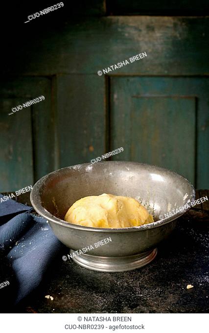 Shortcrust pastry dough in vintage metal bowl over old wooden table. Dark rustic style