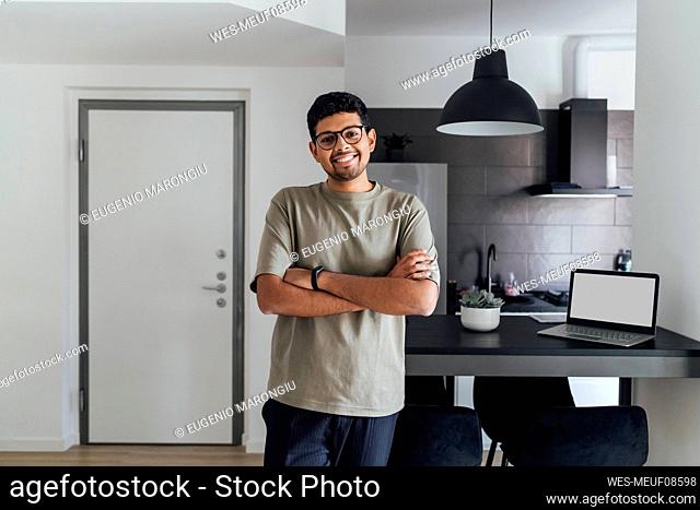 Smiling young man with arms crossed at home