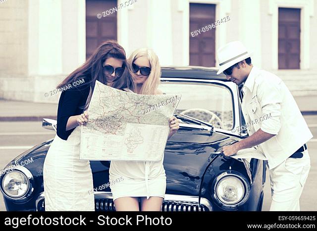 Young fashion people with a road map next to vintage car