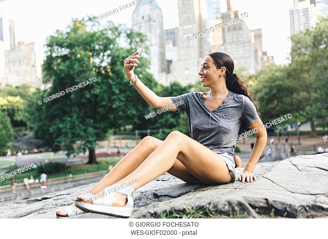 USA, Manhattan, smiling young woman taking selfie with smartphone in Central Park