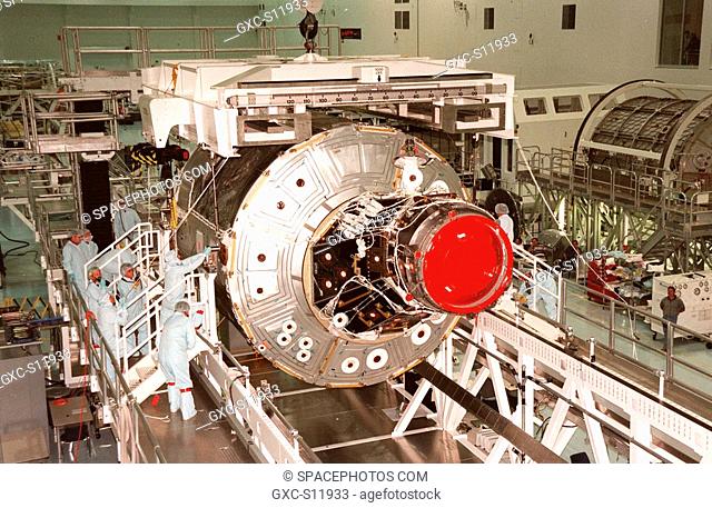 10/22/1998 --- In the Space Station Processing Facility, workers attach the overhead crane that will lift the Unity connecting module from its workstand to move...