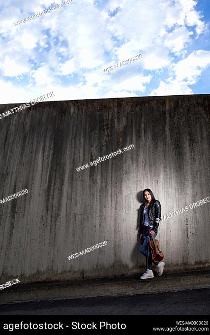 Young female Asian violinist leaning at concrete wall