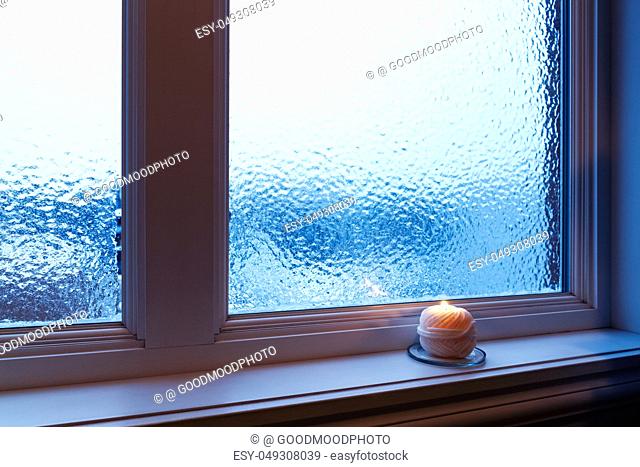 Cozy candle burning near a frosted window. Winter evening