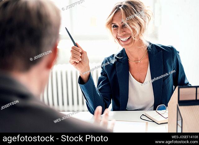 Happy businesswoman holding pen talking with man at office