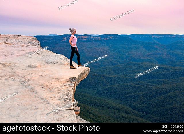 Female stands on the escarpment cliff ledge looking out to the valley below and yonder mountain ranges