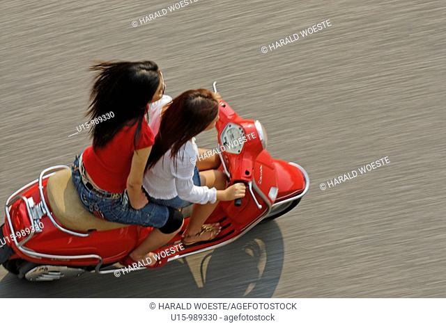 Two fashionable young vietnamese women riding a red Vespa motorbike through the old quarter of Hanoi, Vietnam