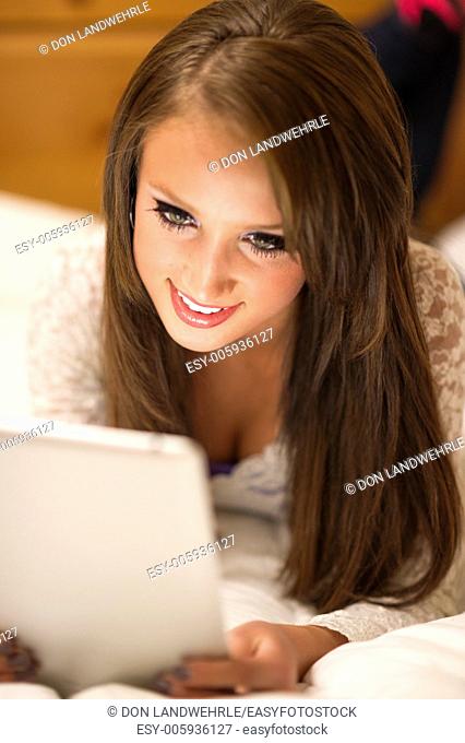 Teenage girl lying on a be working on a tablet computer