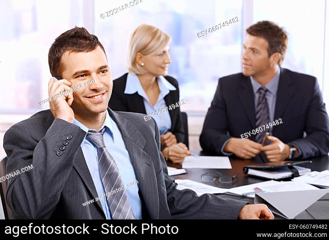 Businessman on phonecall in office meeting with colleagues sitting in background