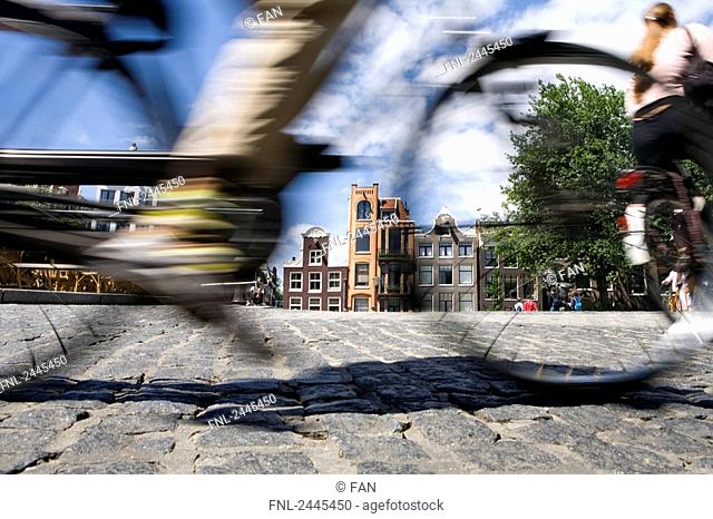Low section view of person cycling with buildings in city, North Holland, Amsterdam, Netherlands