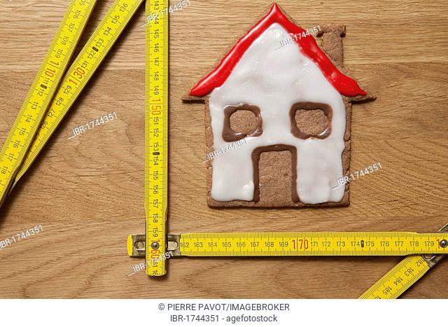 House biscuit with a measuring stick, symbolic image for home construction