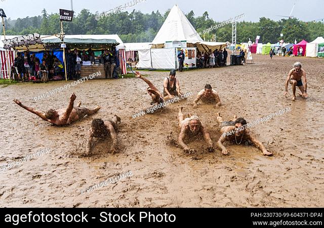 29 July 2023, Hesse, Breitenbach: Festival visitors slide in the mud in pouring rain. The ""Burg Herzberg Festival"" is a music and literature festival and