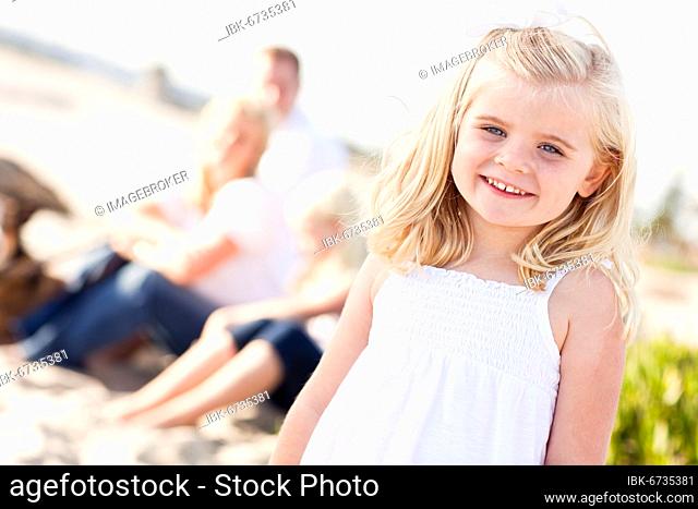 Adorable little blonde girl having fun at the beach with her family