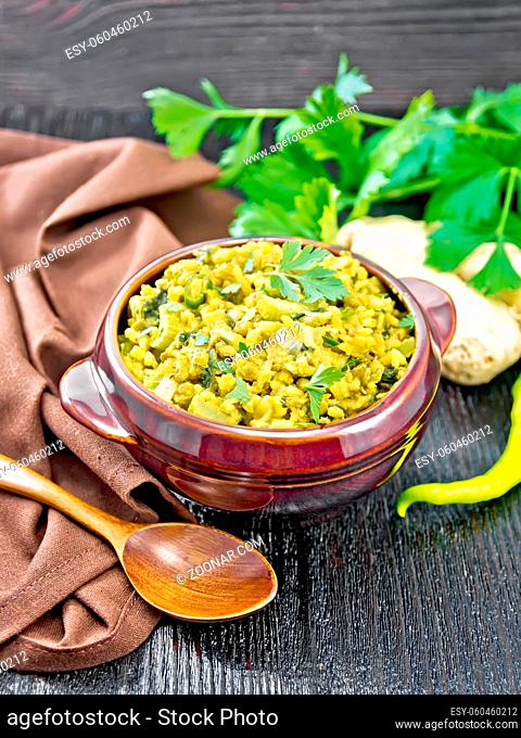 Indian national dish of kichari of mung bean, rice, celery, spinach, hot pepper and spices in a bowl on a napkin, ginger and spoon on wooden board background