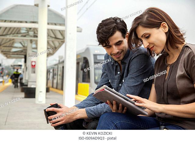 Couple reading newspaper whilst waiting at station, Los Angeles, California, USA
