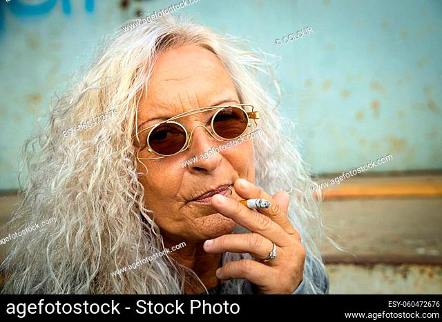 Beautiful woman with long bright curly hair is smoking a cigarette