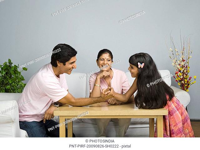 Man arm wrestling with his daughter and his wife watching