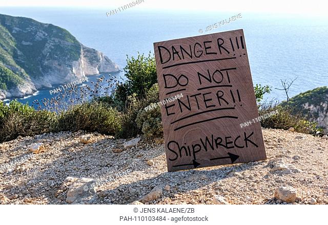 01.10.2018, Greece, Zakynthos: A warning sign ""Danger! Do not enter !!"" stands on the steep coast of Navagio Bay on the Greek island of Zakynthos