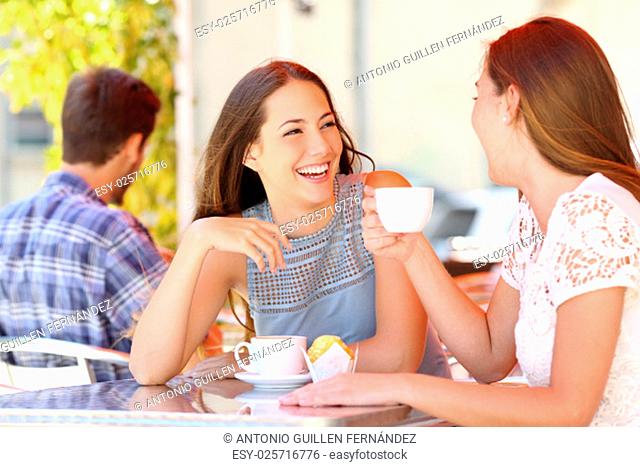 Two friends or sisters talking taking a conversation in a coffee shop terrace looking each other