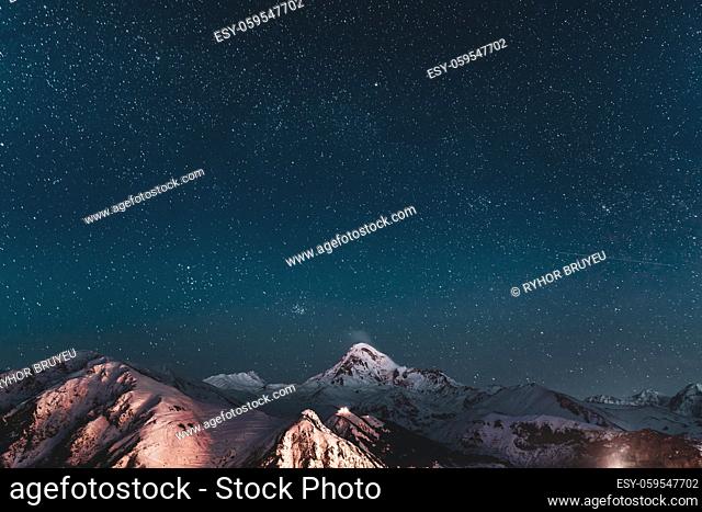Gergeti, Georgia. Winter Night Starry Sky With Glowing Stars Over Peak Of Mount Kazbek Covered With Snow. Beautiful Night Georgian Winter Landscape