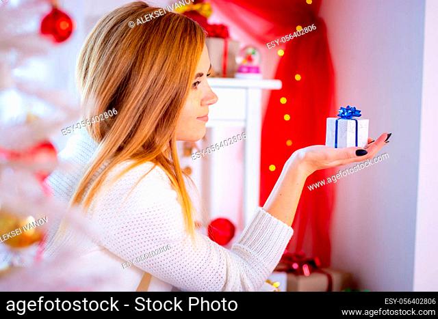 Young girl sits with a small Christmas gift at the Christmas tree, close-up