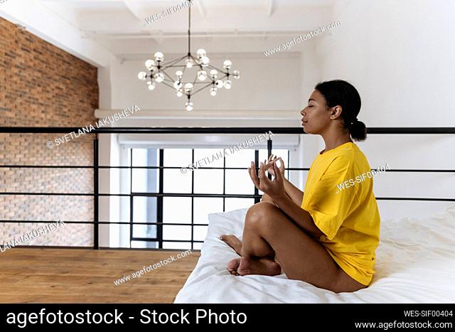 Young woman meditating in the morning sitting cross-legged on bed
