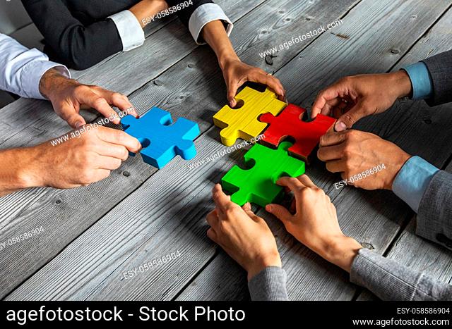 Business people team sitting around meeting table and assembling color jigsaw puzzle pieces unity cooperation ideas concept