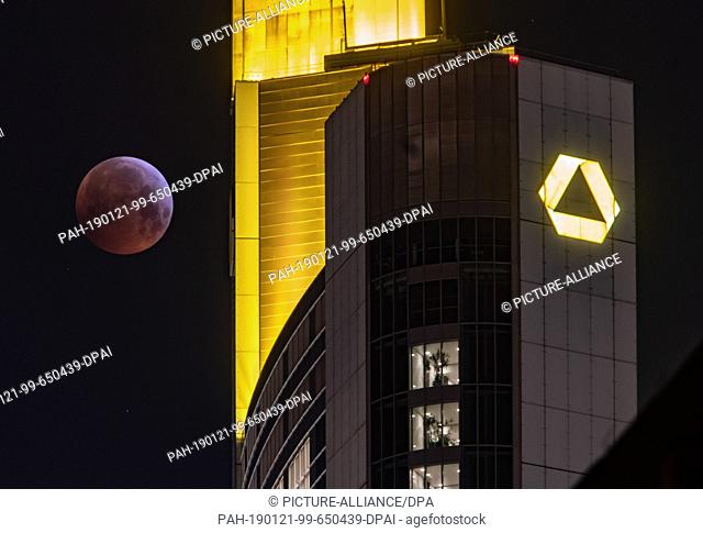 21 January 2019, Hessen, Frankfurt/Main: As a red, so-called ""blood moon"", the full moon stands next to the yellow illuminated Commerbank headquarters