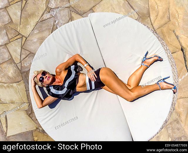 A beautiful mature blonde bikini model poses outdoors near a swimming pool