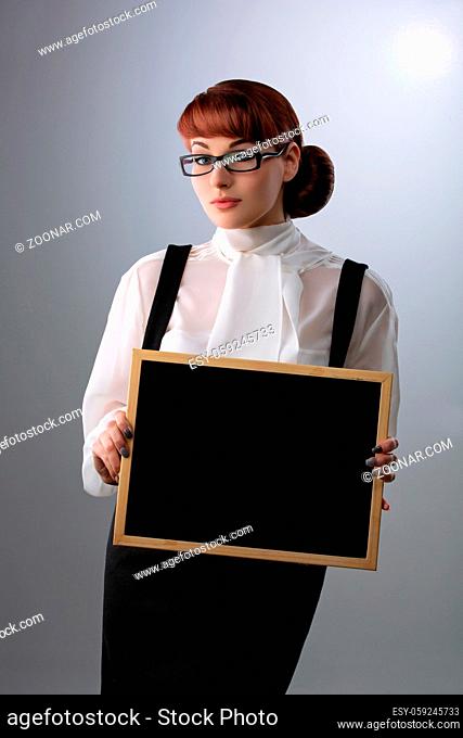 Beautiful young woman in glasses with small blackboard. Teacher wearing blouse and skirt. Copy space. Over grey background