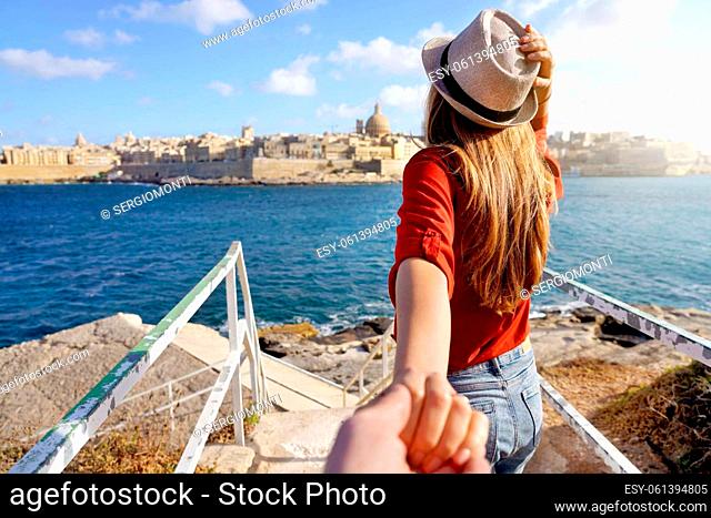 Follow me in Malta. Young carefree tourist woman in hat holds boyfriend hand and looking panoramic view of Valletta, Malta