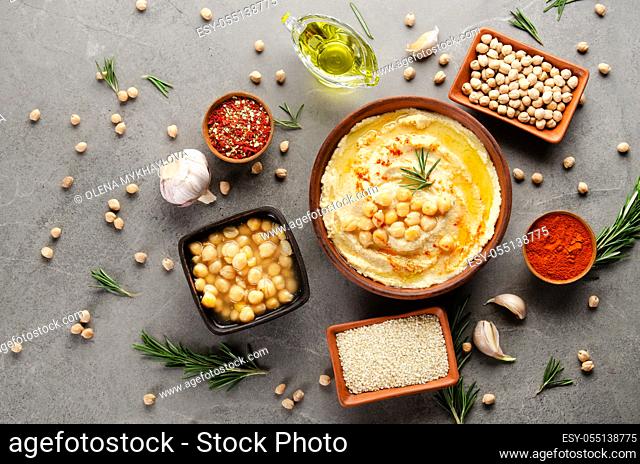 Hummus topped with chickpeas, olive oil and green coriander leaves on stone table with different spices aside. Flat lay