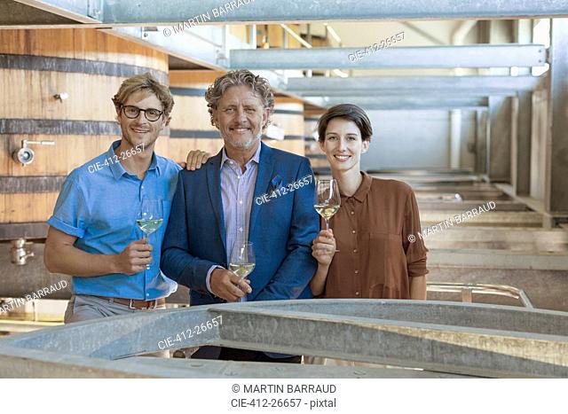 Portrait smiling vintners with white wine in winery cellar