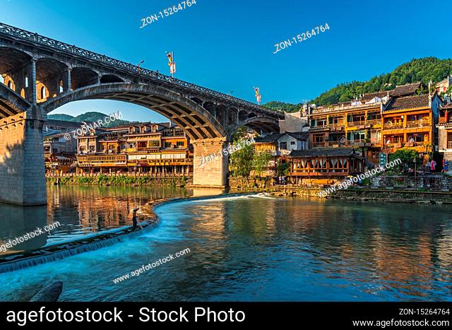Feng Huang, China - August 2019 : Long time exposure of the road bridge over Tuo Jiang river and wooden houses in ancient old town of Fenghuang known as Phoenix