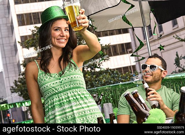 Young woman raising her beer glass while at party on balcony for St Patrick's Day