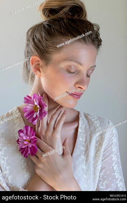 Young beautiful woman with eyes closed holding purple daisy in front of white background