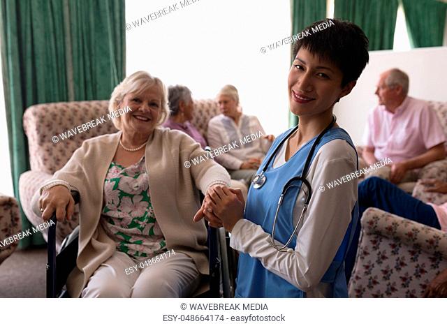 Female doctor holding hands of disabled senior woman in living room