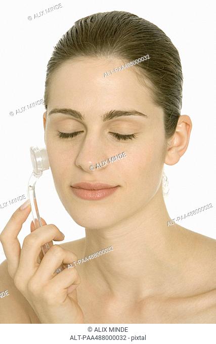 Woman using exfoliator brush on face