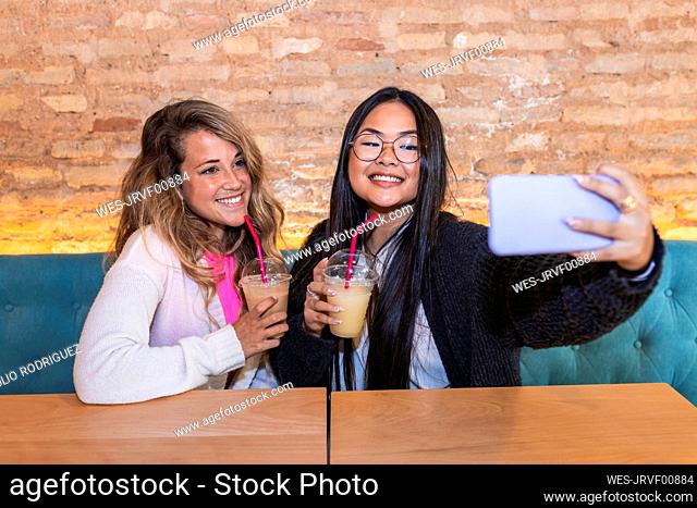 Young woman taking selfie with female friend through mobile phone in bar