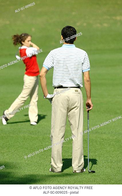 Man watching a woman play a golf shot
