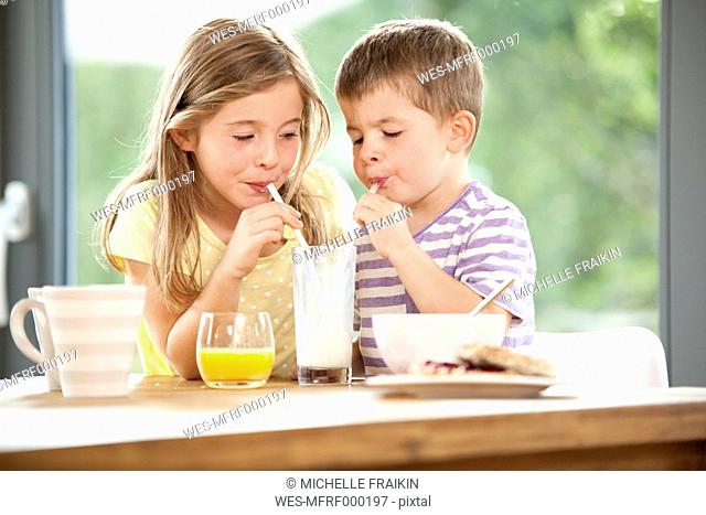 Brother and sister sharing glass of milk