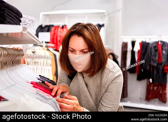 Kundin mit Mundschutz wegen Covid-19 Pandemie bei Mode Auswahl in einer Boutique
