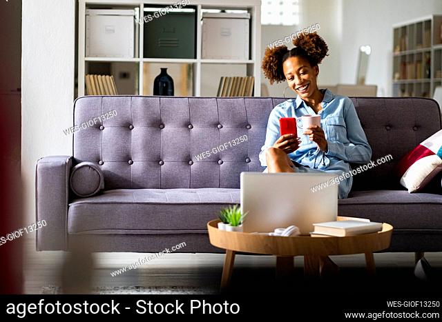 Young woman on video call through smart phone while having coffee in living room