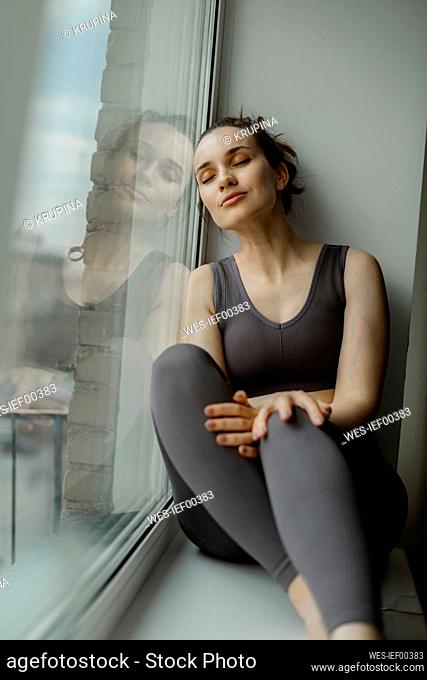 Woman with eyes closed relaxing on window sill at home