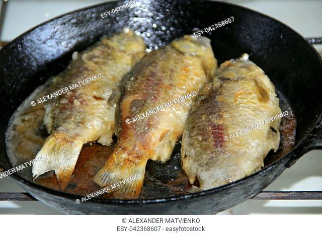 Three fried crucian on griddle. Cooking fried fish. Dish of fried crucians. Delicious river fish