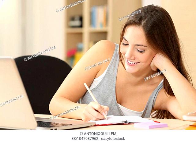 Happy student taking notes in an agenda sitting at a desk at home