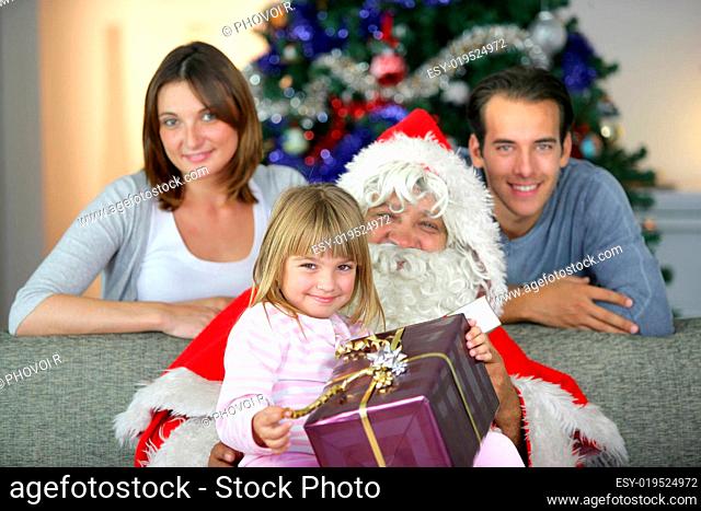 Portrait of a smiling girl with a gift sitting on Santa's lap